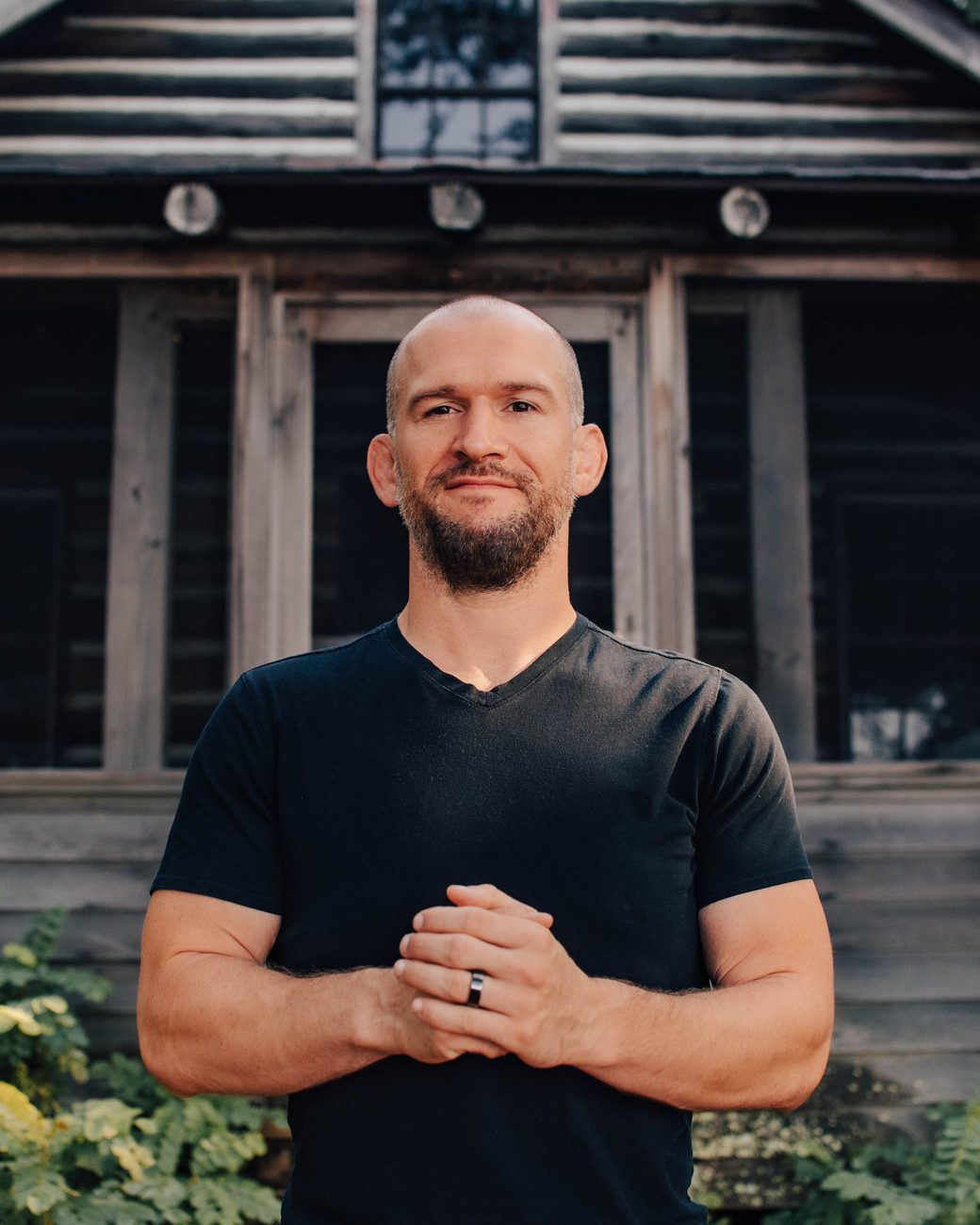 Chris Matakas standing outside a log cabin in the woods, smiling
